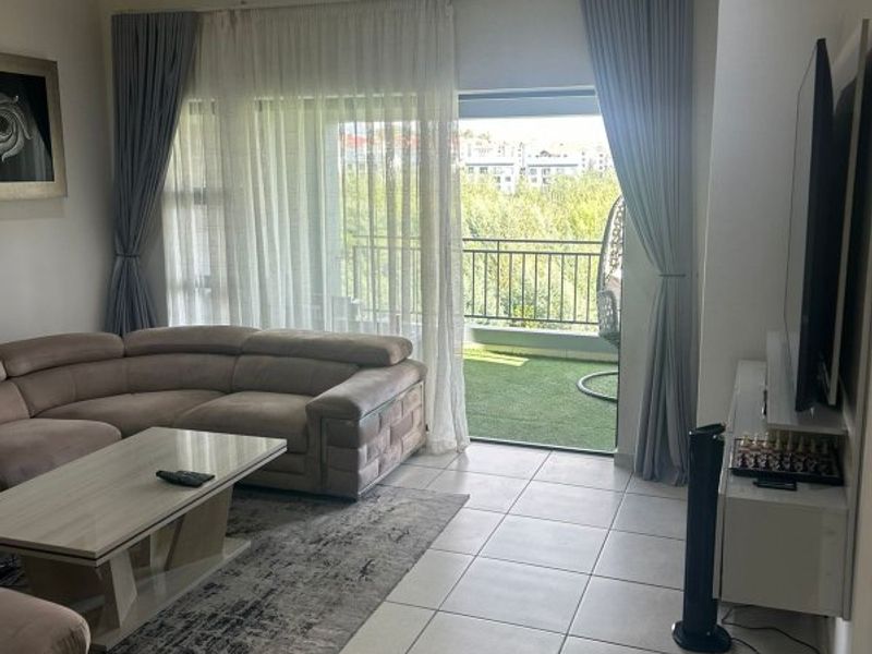 Spacious living room featuring neutral tiled flooring, recessed lighting, and large sliding glass doors providing direct access to a private balcony.