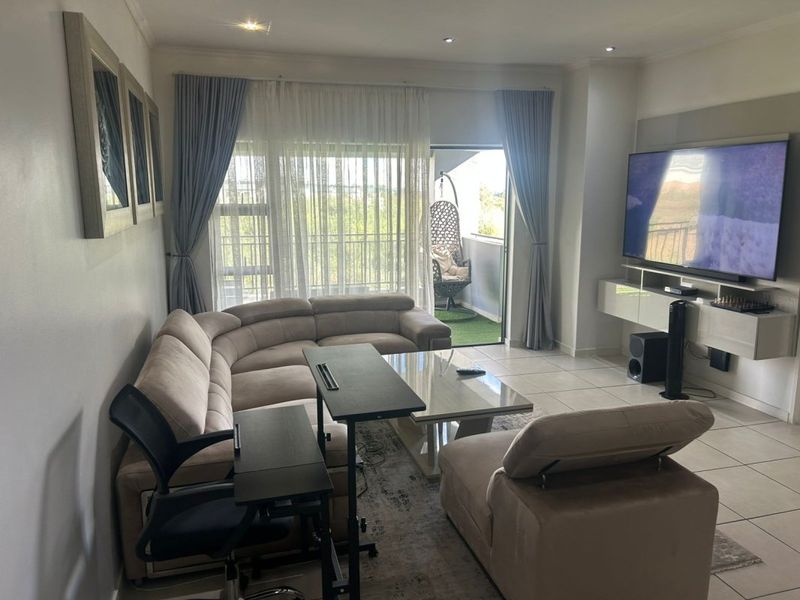 A well-maintained living room featuring tiled flooring, recessed lighting, and a built-in media console, with direct access to a private balcony.