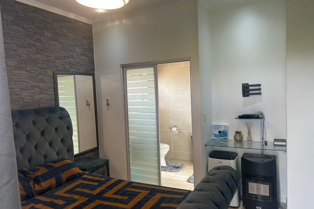 A bedroom featuring a stone veneer accent wall, recessed lighting, and an en-suite bathroom accessed via a sliding door.