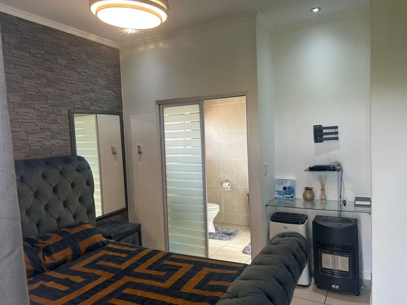 A bedroom featuring a stone veneer accent wall, recessed lighting, and an en-suite bathroom accessed via a sliding door.