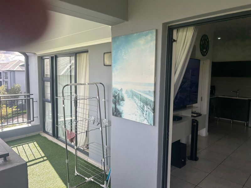 A covered balcony featuring artificial grass flooring and sliding glass doors, providing a seamless transition to the interior living space.