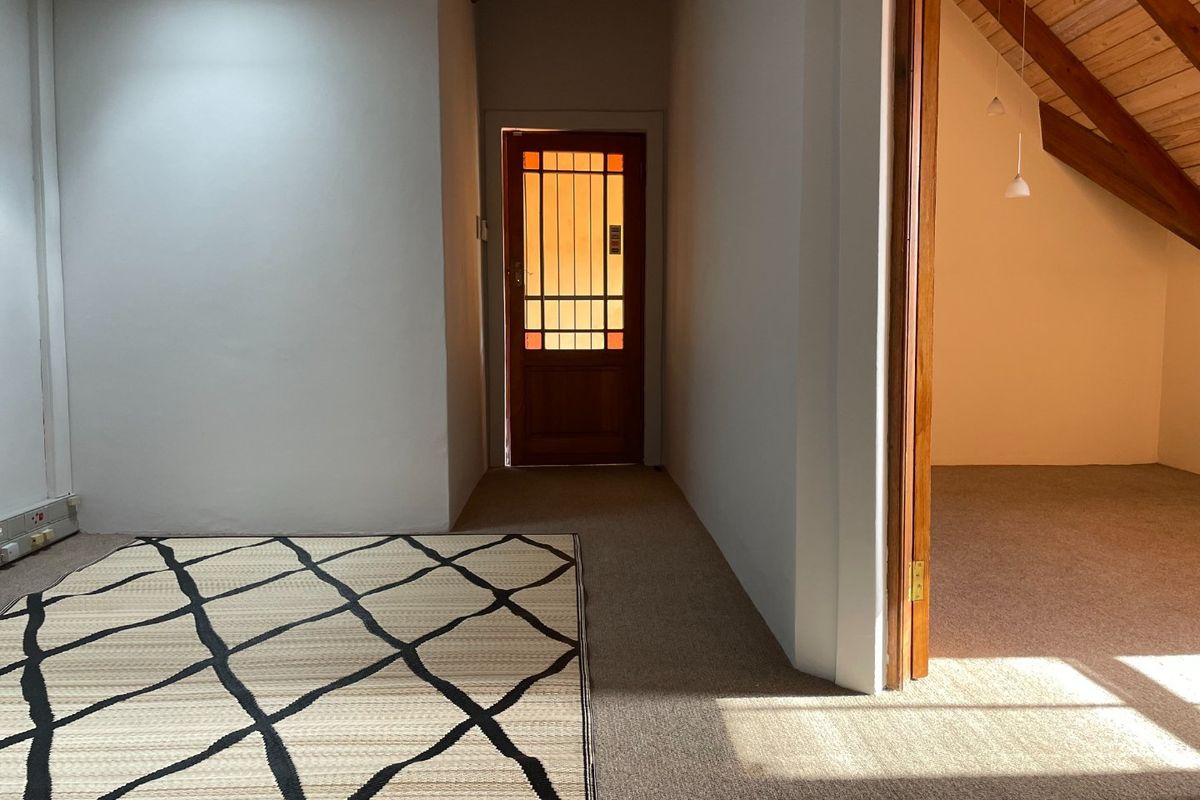 A bright, carpeted hallway featuring exposed timber rafters and a secure timber entrance door with decorative glass panels.