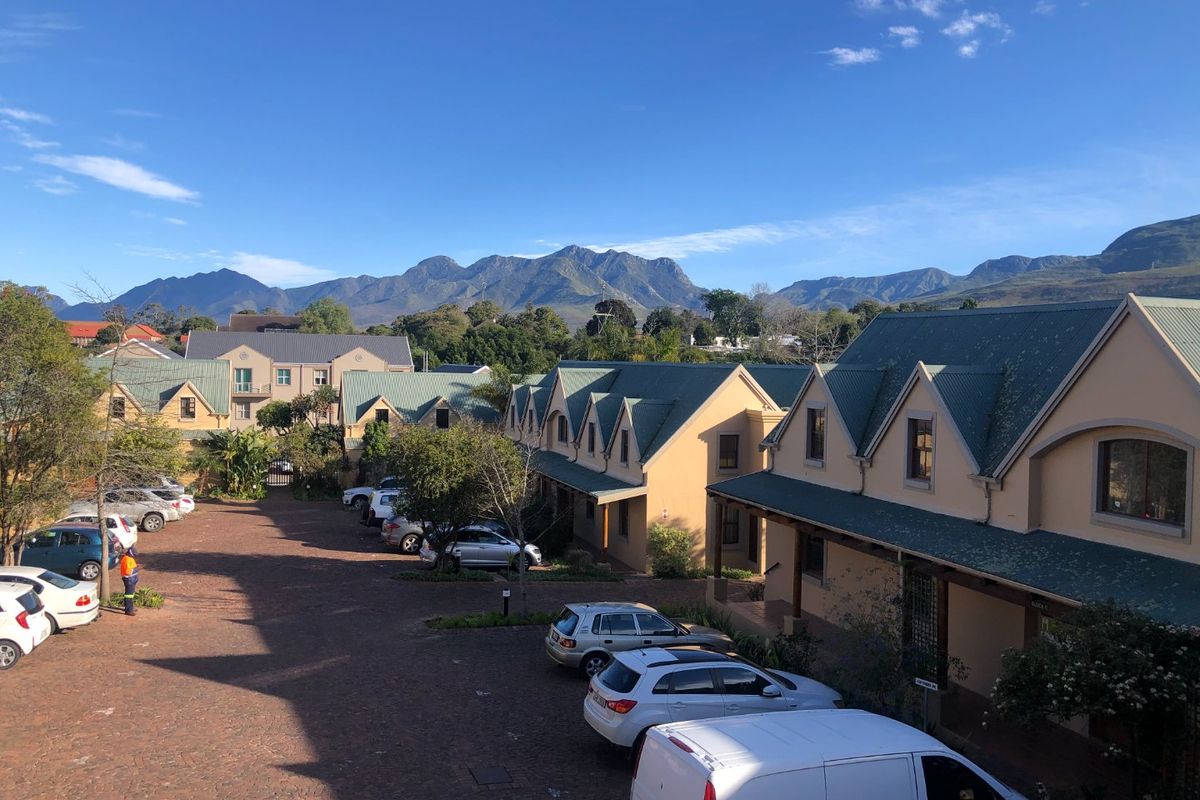 Elevated view of a commercial office complex featuring multiple buildings with pitched roofs, gabled dormers, and a paved parking area against a mountain backdrop.