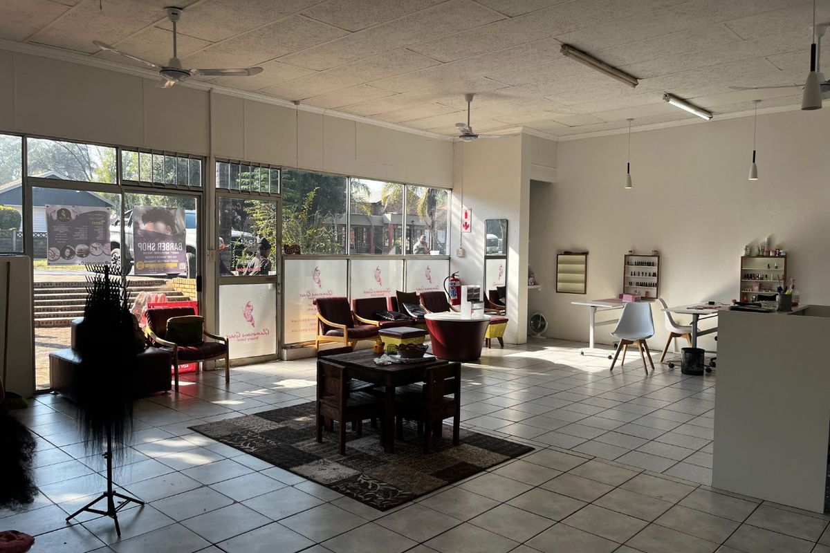 Spacious open-plan commercial retail or salon space featuring large glass storefront windows, tiled flooring, and suspended ceiling with integrated lighting.