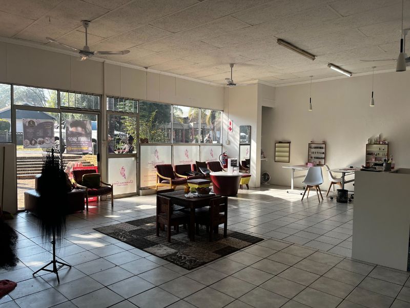 Spacious open-plan commercial retail or salon space featuring large glass storefront windows, tiled flooring, and suspended ceiling with integrated lighting.