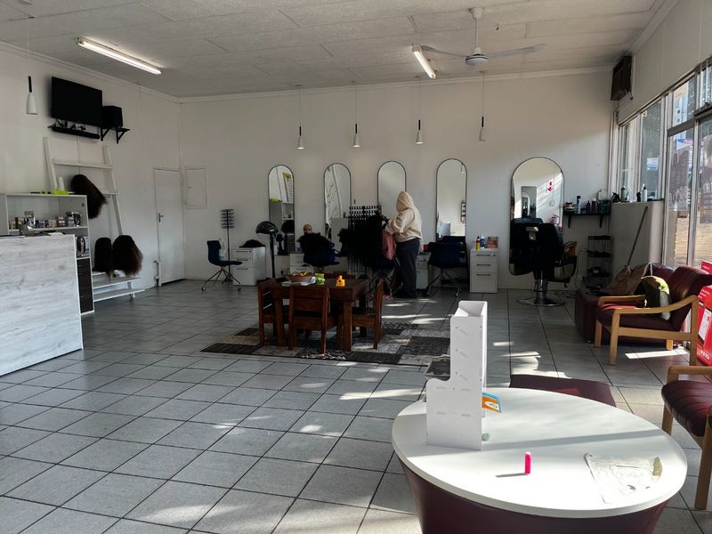 Open-plan commercial salon space featuring tiled flooring, multiple wall-mounted styling mirrors, and a reception area with functional lighting and ceiling fan.