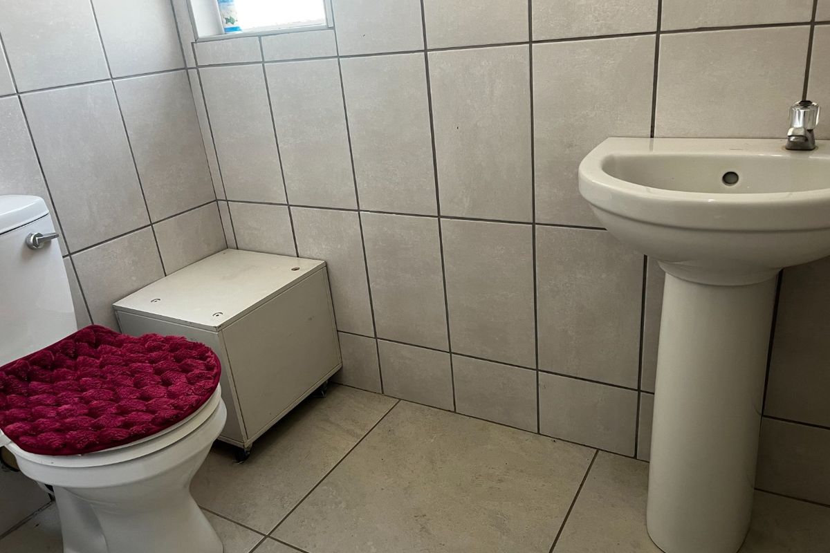 A clean, functional bathroom featuring a pedestal washbasin, standard toilet, and neutral ceramic wall and floor tiling.