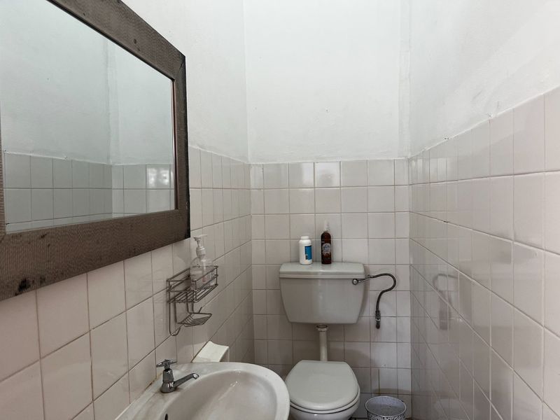 A compact commercial bathroom featuring white ceramic wall tiles, a pedestal sink, and a standard flush toilet.