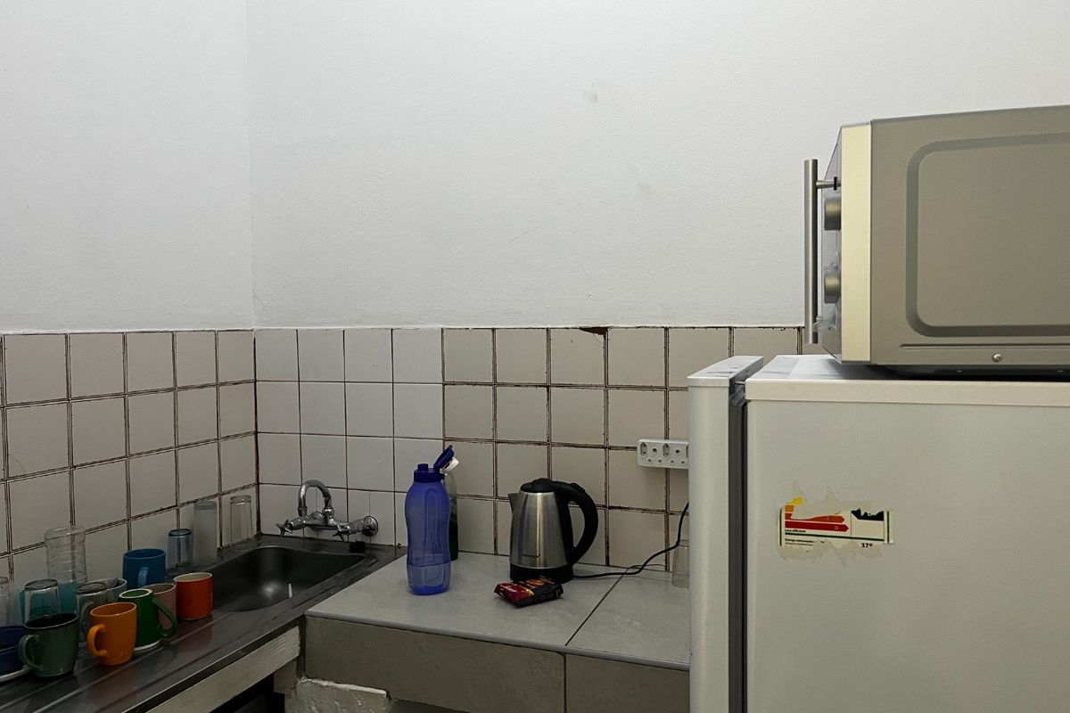 A compact kitchen area featuring a stainless steel sink, tiled backsplash, and built-in counter space, suitable for basic utility or staff room use.