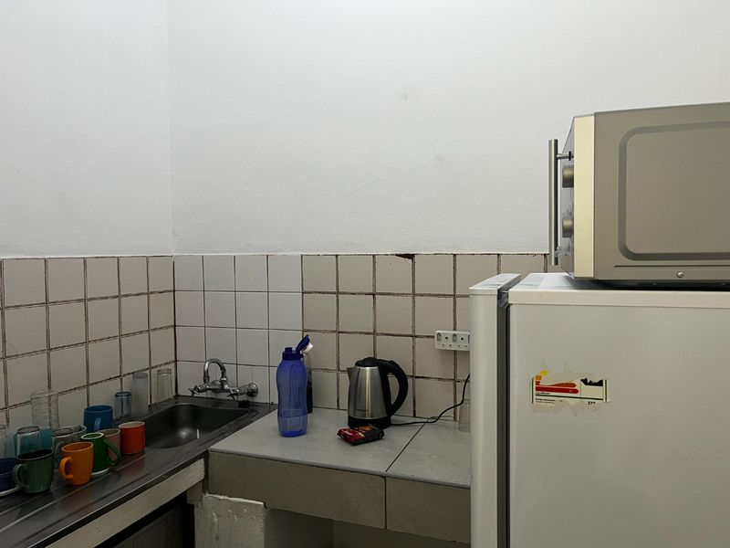A compact kitchen area featuring a stainless steel sink, tiled backsplash, and built-in counter space, suitable for basic utility or staff room use.