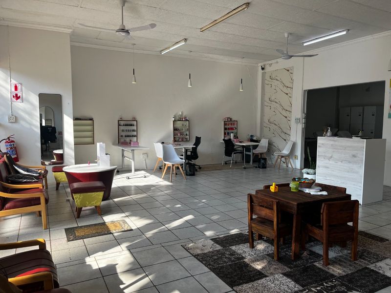 Open-plan commercial space featuring tiled flooring, ceiling fans, and a reception counter, suitable for a salon or retail environment.