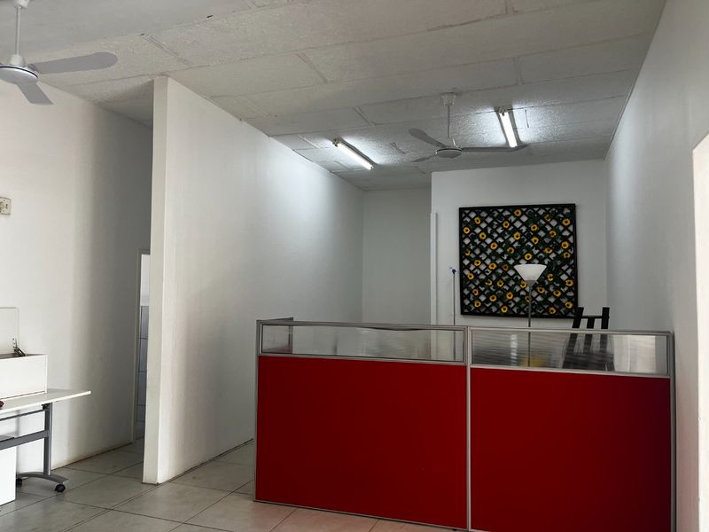 A functional commercial office space featuring tiled flooring, partition walls, and suspended ceiling with integrated lighting and fans.