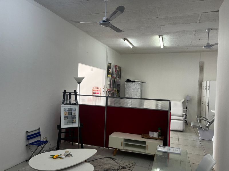 Commercial office space featuring tiled flooring, ceiling fans, fluorescent lighting, and built-in storage lockers, currently partitioned for multi-use functionality.