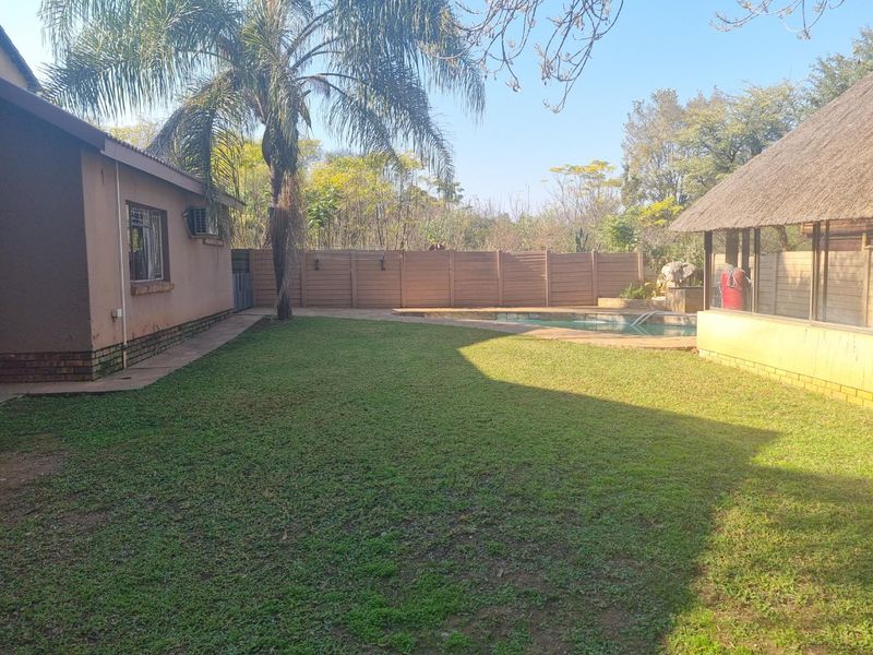 Spacious rear garden featuring a swimming pool, paved surround, and a thatched lapa, providing a functional outdoor entertainment area.