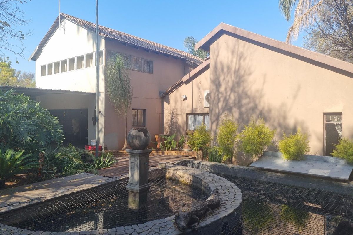 Rear exterior view of the house featuring a paved patio area, a decorative pond with a fountain, and established garden landscaping.
