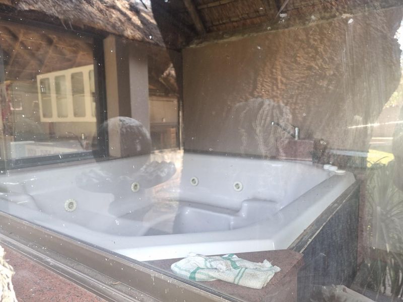 A built-in spa bath located within a room featuring a thatched roof, viewed through a dirty window.