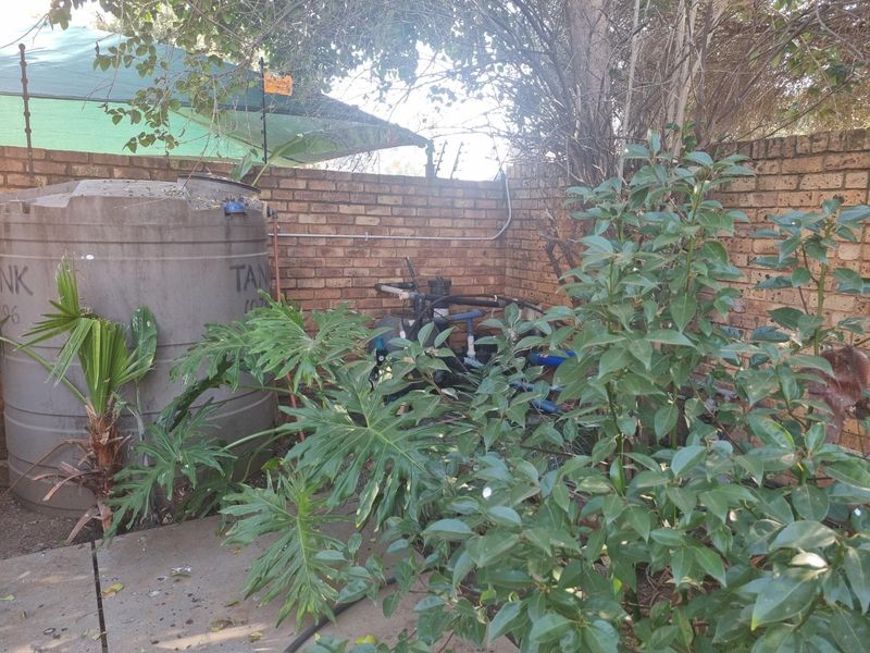 Utility area featuring a water storage tank and pool pump equipment enclosed by a brick boundary wall with electric fencing.
