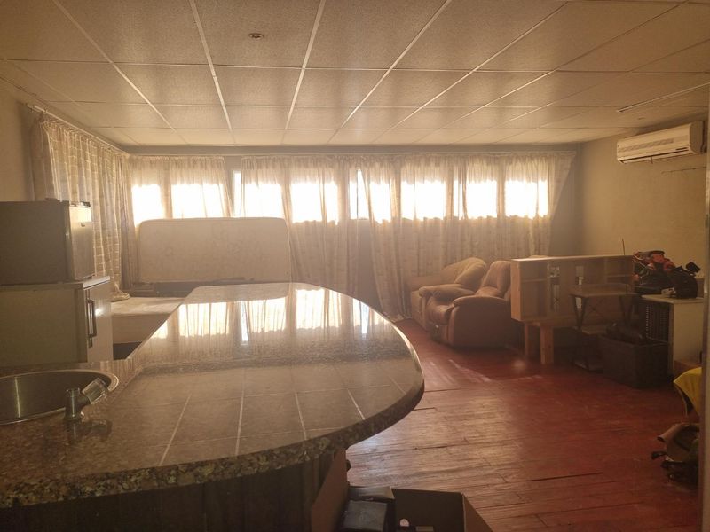 Open plan living and kitchen area featuring timber flooring, a tiled breakfast bar, and a drop ceiling with integrated air conditioning.