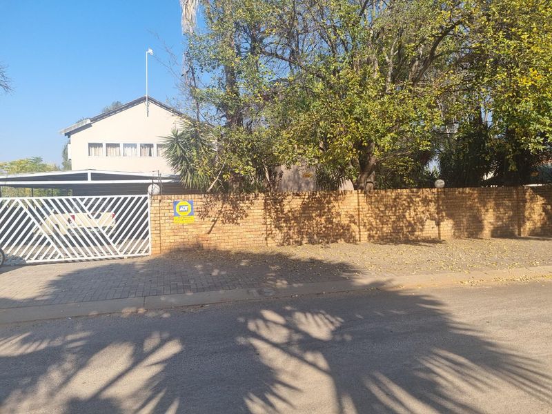 Front exterior view of the property featuring a brick boundary wall, metal driveway gate, and a covered carport area.