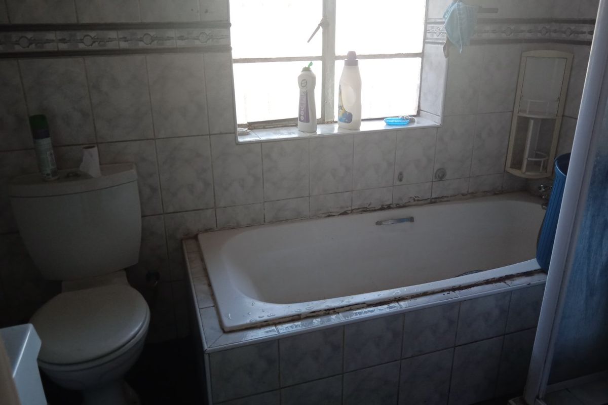 A dated bathroom featuring a built-in bathtub and toilet with tiled walls, requiring maintenance to the sealant and grout.