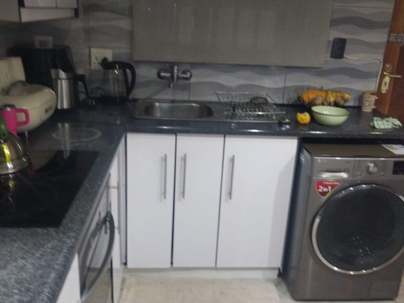 A functional kitchen area featuring white cabinetry, dark laminate countertops, a stainless steel sink, and an integrated washing machine.