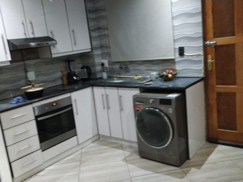 A functional kitchen featuring white cabinetry, dark countertops, a built-in oven, extractor fan, and tiled finishes throughout.