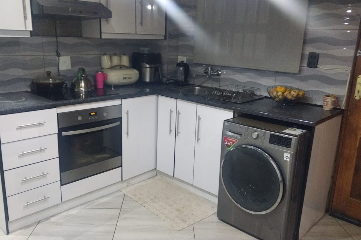 Compact kitchen featuring white cabinetry, dark laminate countertops, built-in oven, extractor fan, and tiled backsplash with integrated laundry appliance space.