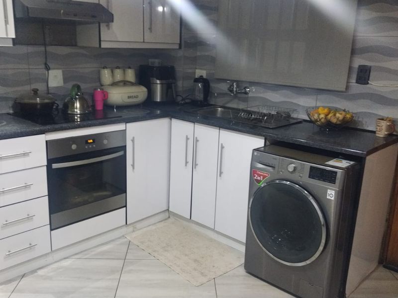 Compact kitchen featuring white cabinetry, dark laminate countertops, built-in oven, extractor fan, and tiled backsplash with integrated laundry appliance space.