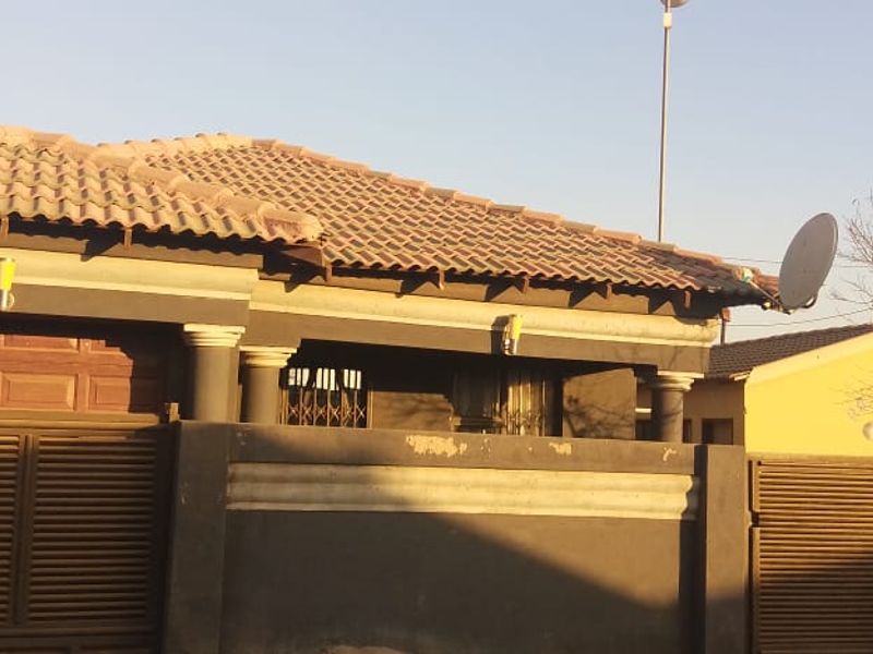 Front elevation of a residential house featuring a tiled roof, boundary wall with metal gate, and integrated garage access.