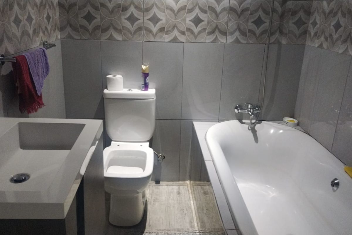 A modern bathroom featuring a built-in vanity, ceramic basin, toilet, and a bathtub with tiled walls and flooring.