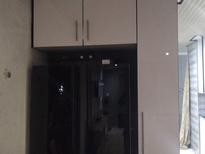 A kitchen area featuring built-in cabinetry and overhead storage cupboards, with an integrated fridge housing unit.