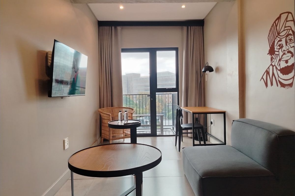 A modern living room featuring tiled floors, recessed lighting, and direct access to a balcony through a glass door.