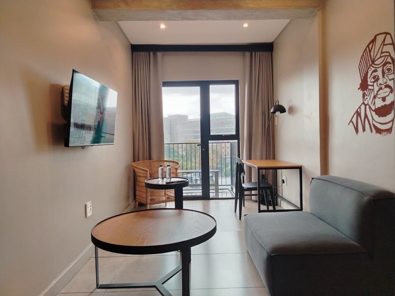 A modern living room featuring tiled floors, recessed lighting, and direct access to a balcony through a glass door.