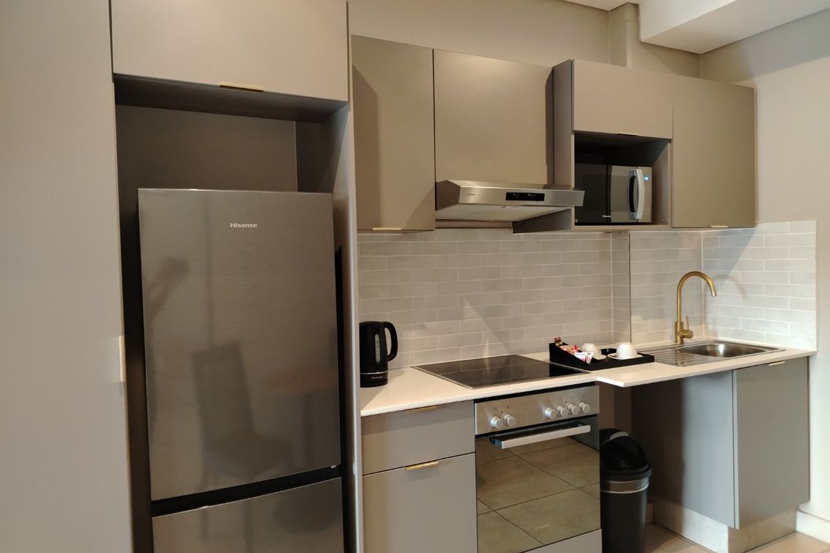 Modern kitchen featuring sleek grey cabinetry, stone countertops, subway tile backsplash, and integrated stainless steel appliances with a stylish brass faucet.