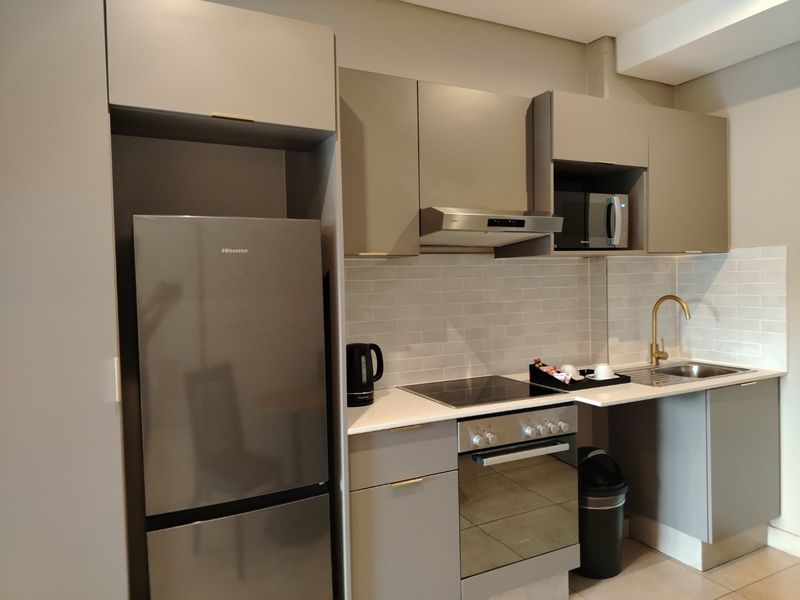 Modern kitchen featuring sleek grey cabinetry, stone countertops, subway tile backsplash, and integrated stainless steel appliances with a stylish brass faucet.