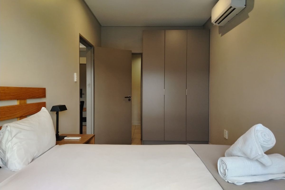 A well-maintained bedroom featuring built-in cupboards, recessed downlighting, and a wall-mounted split-system air conditioner.