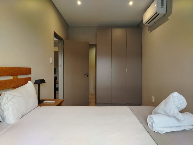 A well-maintained bedroom featuring built-in cupboards, recessed downlighting, and a wall-mounted split-system air conditioner.