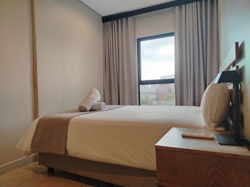 A well-maintained bedroom featuring neutral tones, tiled flooring, and a window with floor-to-ceiling curtains, providing a comfortable and functional living space.