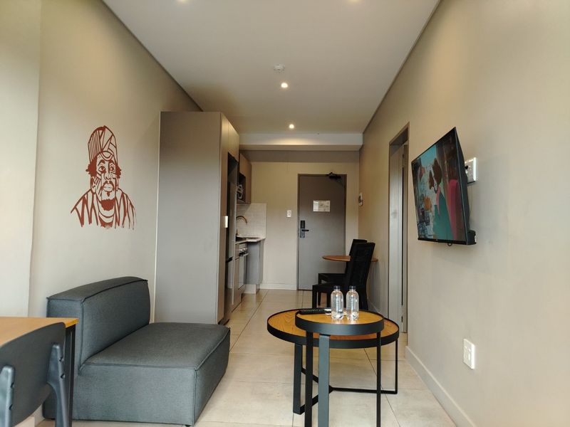 Open-plan living area featuring tiled flooring, recessed lighting, and a compact kitchenette with built-in cabinetry.