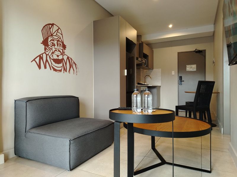 Compact open-plan apartment living area featuring a kitchenette with built-in cabinetry, modern tiled flooring, and recessed lighting.