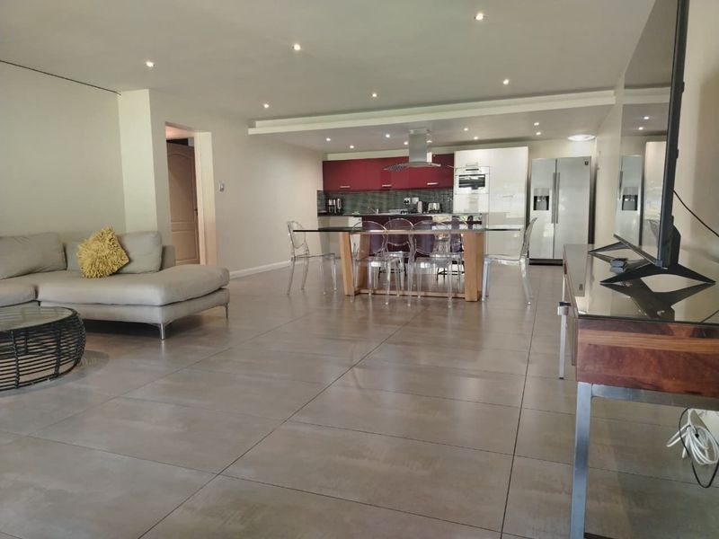 Spacious open-plan living area featuring large format floor tiles, recessed lighting, and a modern kitchen with built-in cabinetry and integrated appliances.