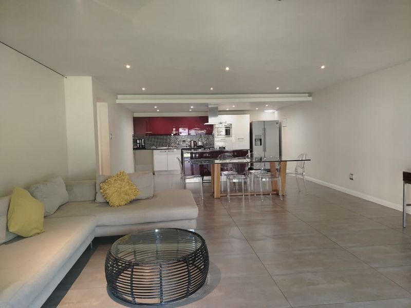 Spacious open-plan living and dining area featuring large format floor tiles, recessed lighting, and a modern kitchen with built-in cabinetry and appliances.