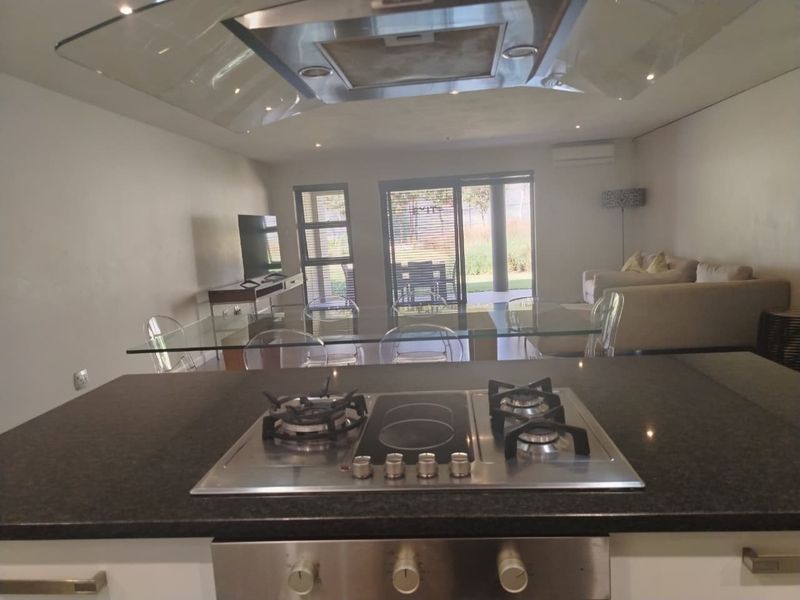 Modern open-plan living area featuring a kitchen island with a dual gas and electric hob, integrated oven, and seamless flow to the outdoor patio.