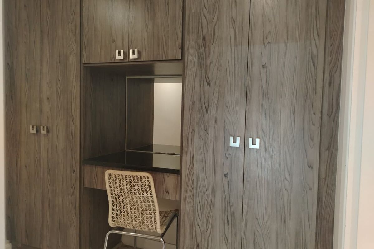 A bedroom featuring extensive floor-to-ceiling wood-grain built-in cabinetry with an integrated vanity station and stone countertop.