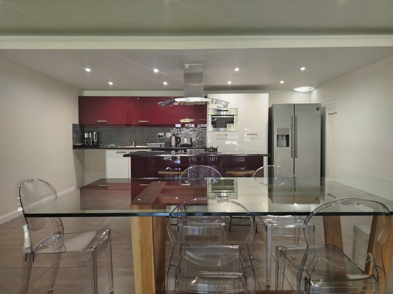 Modern open-plan kitchen featuring high-gloss cabinetry, a central island, integrated appliances, and a mosaic tile backsplash, seamlessly flowing into the dining area.