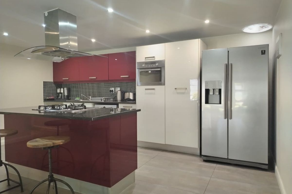 Modern kitchen featuring a central island with gas hob, stainless steel extractor, built-in oven, and high-gloss cabinetry with tiled splashback.