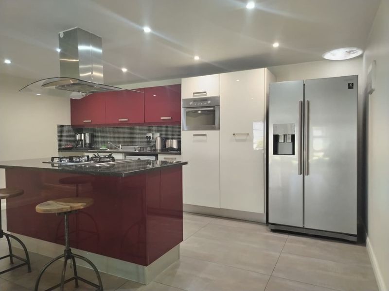 Modern kitchen featuring a central island with gas hob, stainless steel extractor, built-in oven, and high-gloss cabinetry with tiled splashback.