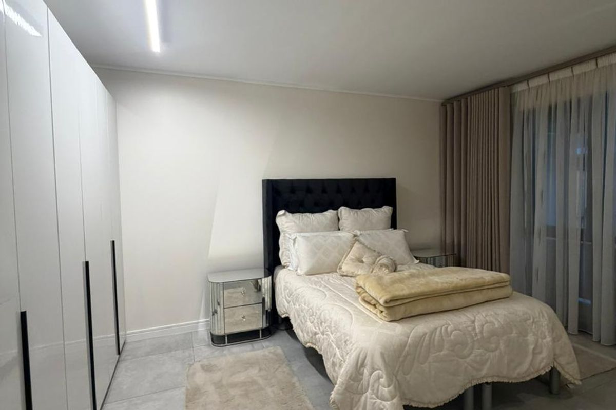 A modern bedroom featuring large format floor tiles, sleek white built-in wardrobes, and a contemporary linear ceiling light fixture.