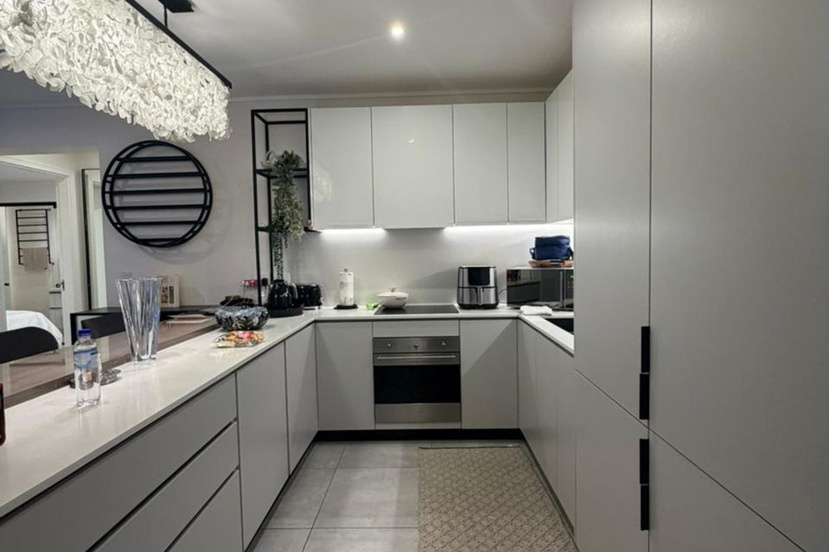 A modern, well-appointed kitchen featuring sleek handleless cabinetry, stone countertops, integrated appliances, and large format floor tiles with elegant pendant lighting.