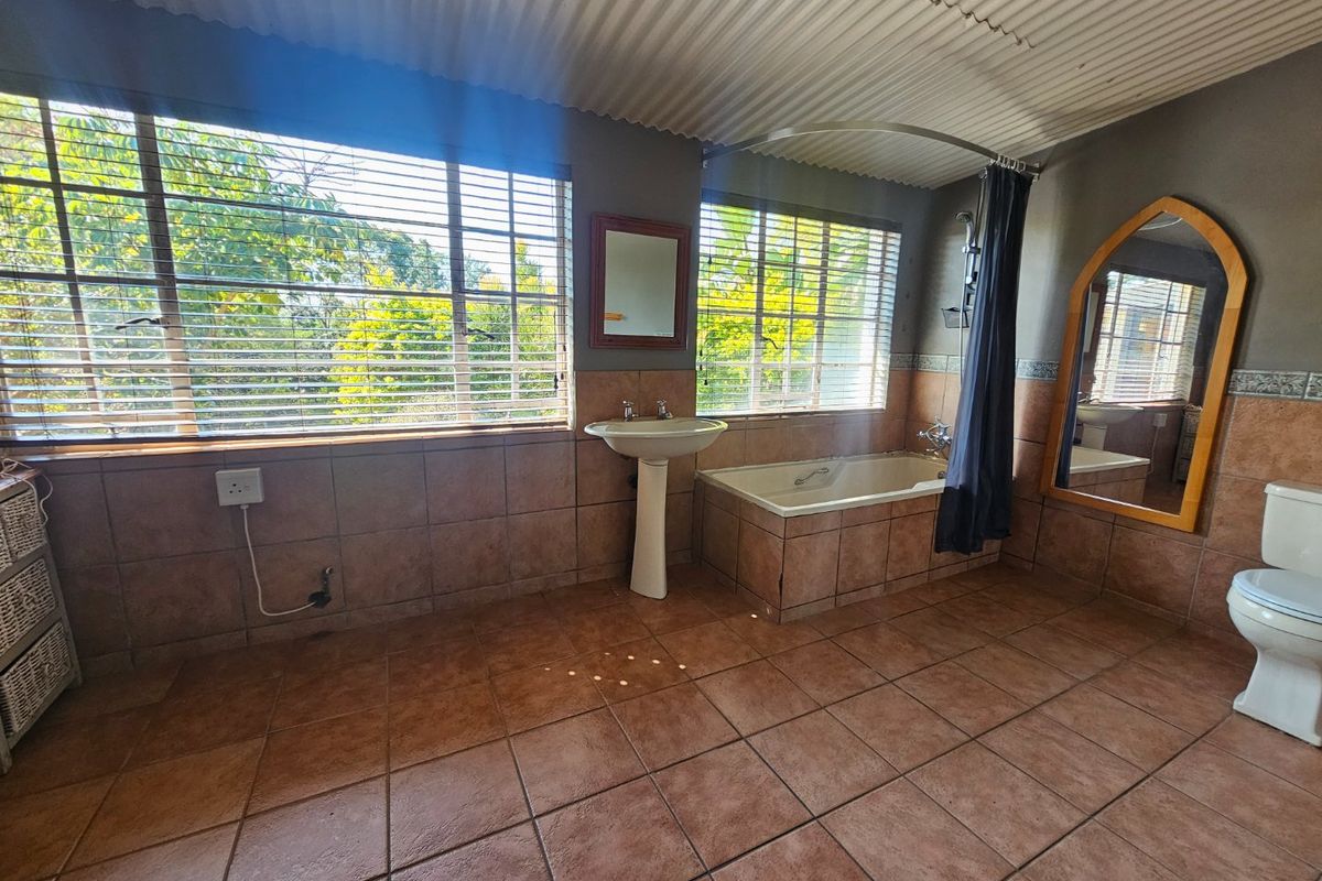 Spacious bathroom featuring a pedestal basin, built-in bathtub with shower curtain, and tiled finishes throughout, offering potential for a modern renovation.